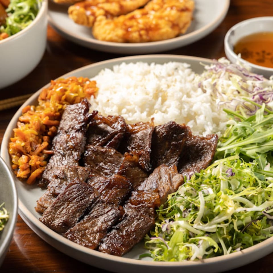 A Korean BBQ plate with grilled beef, white rice, kimchi, and a fresh green salad.
