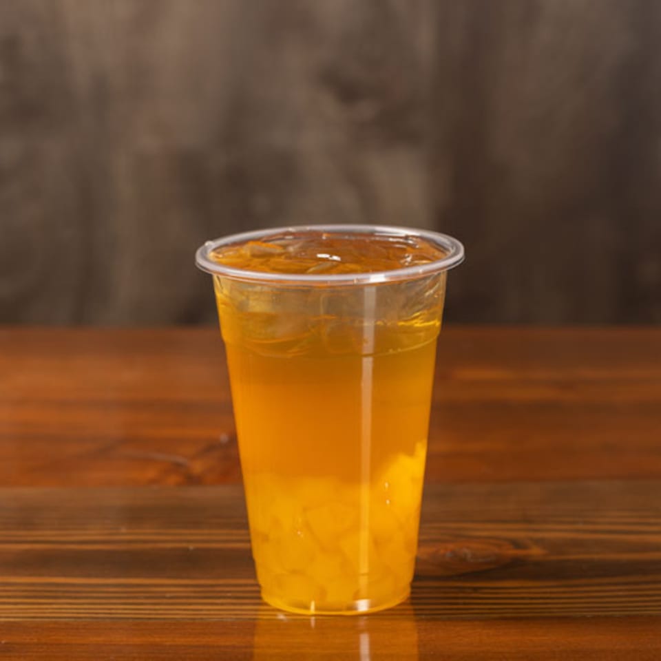 A plastic cup of iced Korean tea with fruit pieces sits on a wooden table.