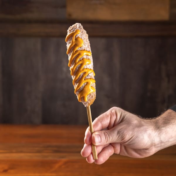Hand holding a Korean corn dog topped with sugar and drizzled with yellow mustard.