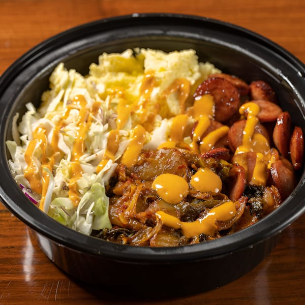 A Korean BBQ bowl with sausage, kimchi, coleslaw, and potato salad, drizzled with sauce.