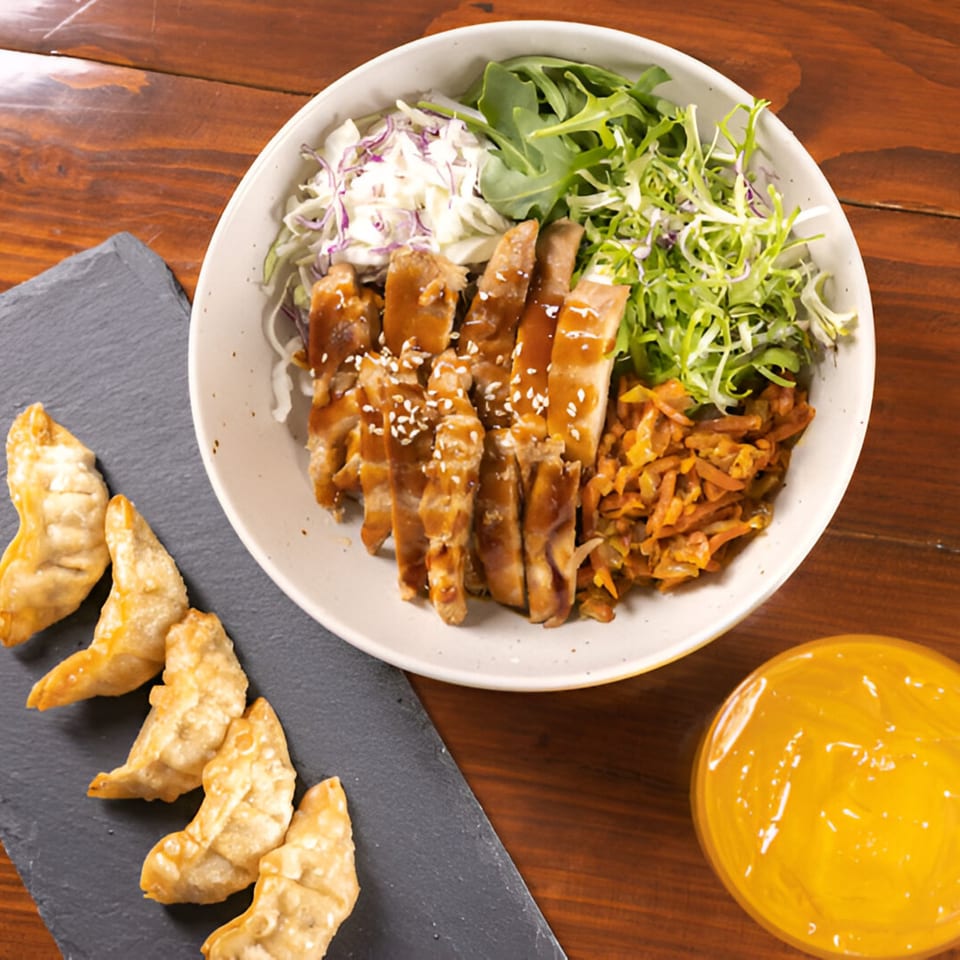 A Korean BBQ bowl with sliced chicken, salad, kimchi, and a side of fried dumplings and sauce.