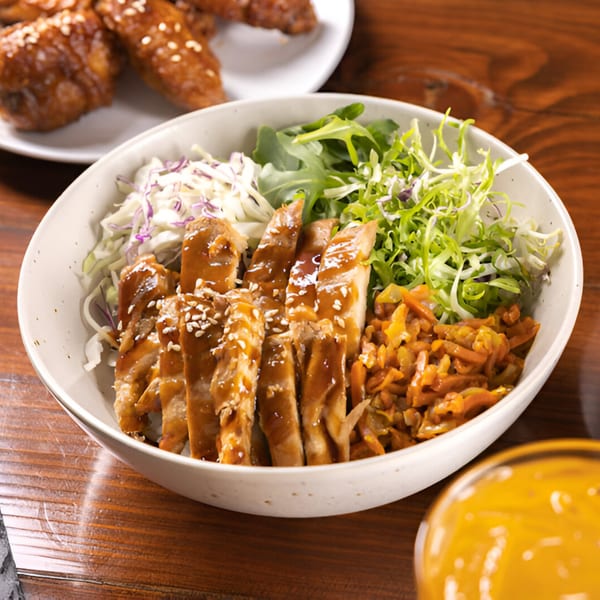 Korean BBQ chicken rice bowl with shredded cabbage, greens, and kimchi on a wooden table.