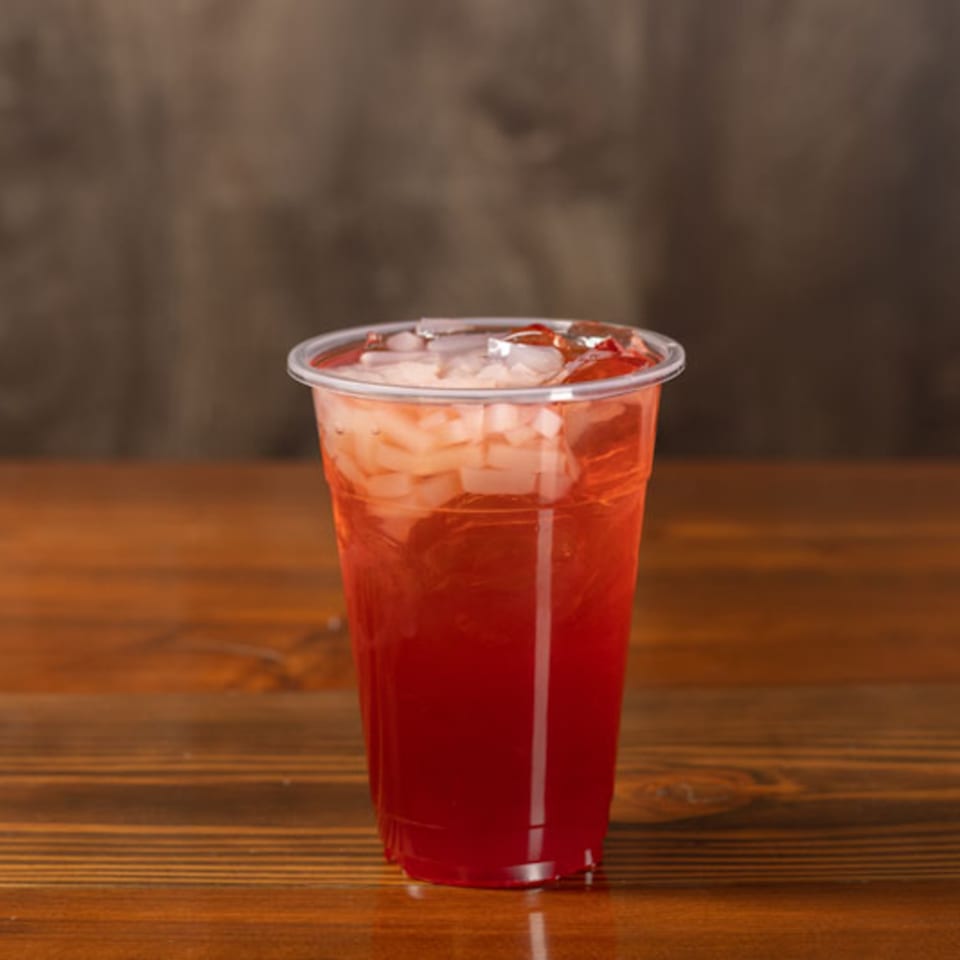 Red iced drink with white jelly cubes in a clear plastic cup on a wooden table.