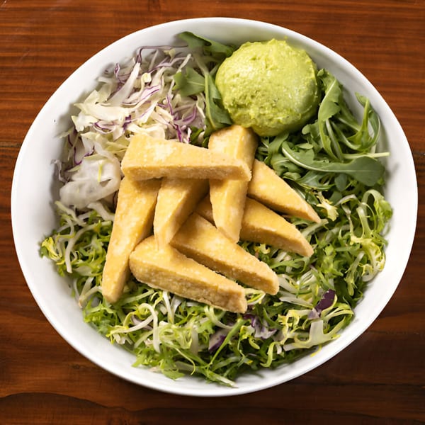 A white bowl of Korean salad with fried tofu, shredded cabbage, mixed greens, and guacamole.